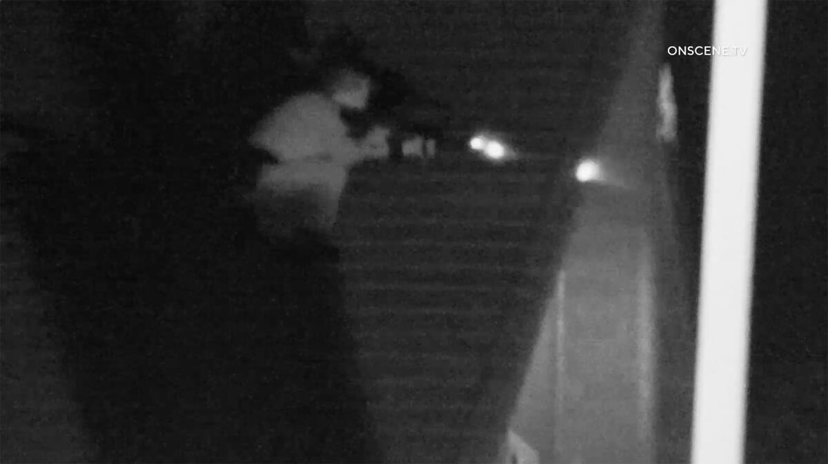 An officer crouches on a house roof in the dark.