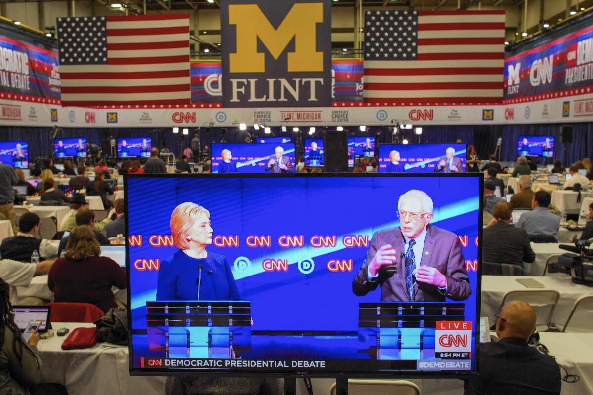 A debate between Hillary Clinton and Bernie Sanders is seen on a TV in the press room in Flint, Mich.