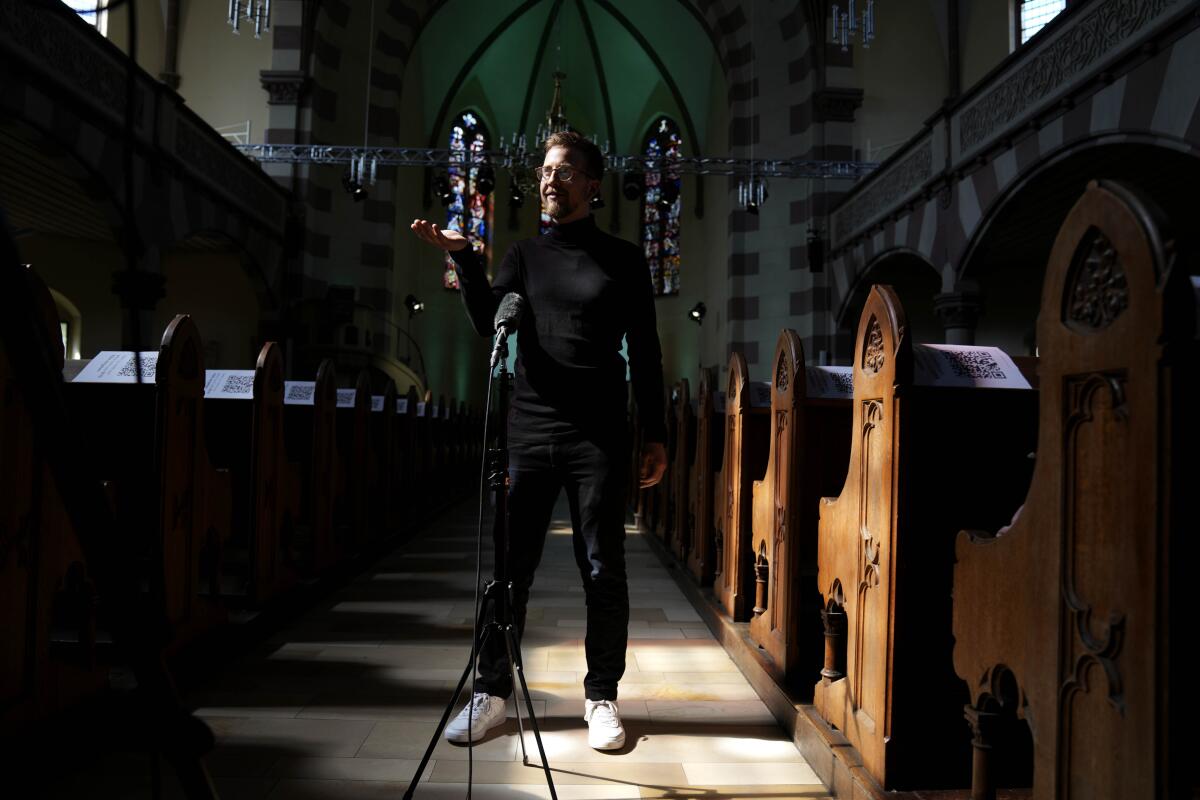 A man stands in the aisle of a church and gestures.  