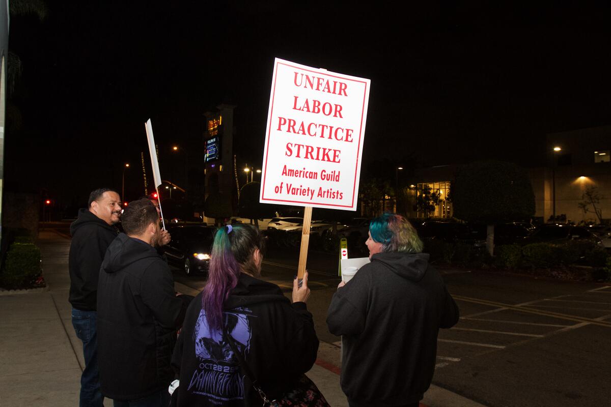 Four people stand, backs to camera, holding picket signs and fliers at night.