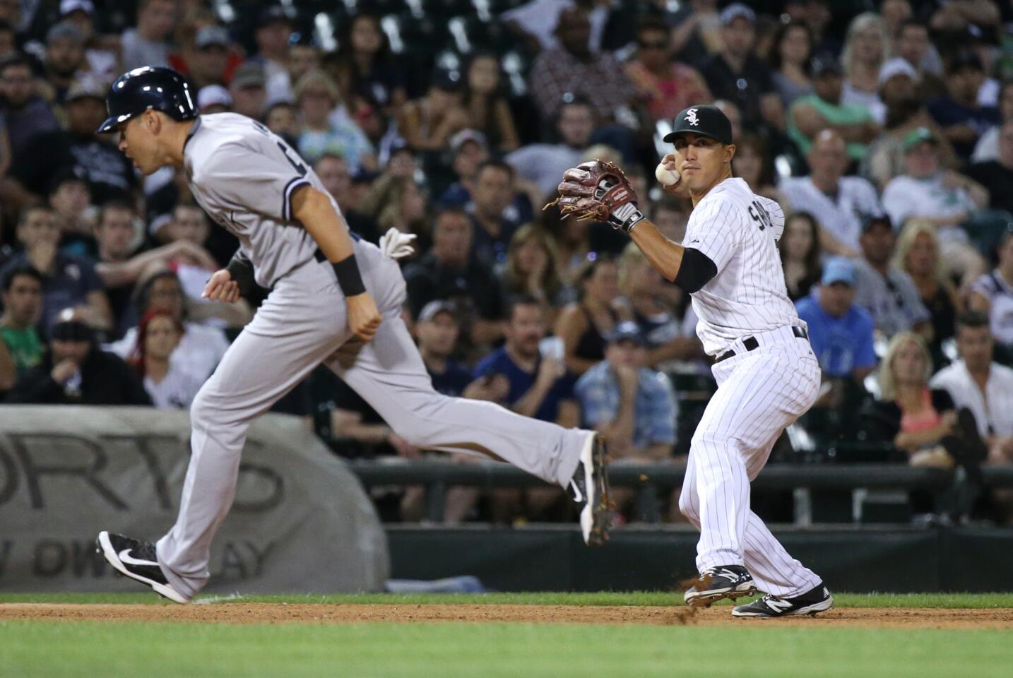 White Sox third baseman Tyler Saladino, right, winds up for the throw to first base as New York Yankees center fielder Jacoby Ellsbury heads for third base in the sixth inning.