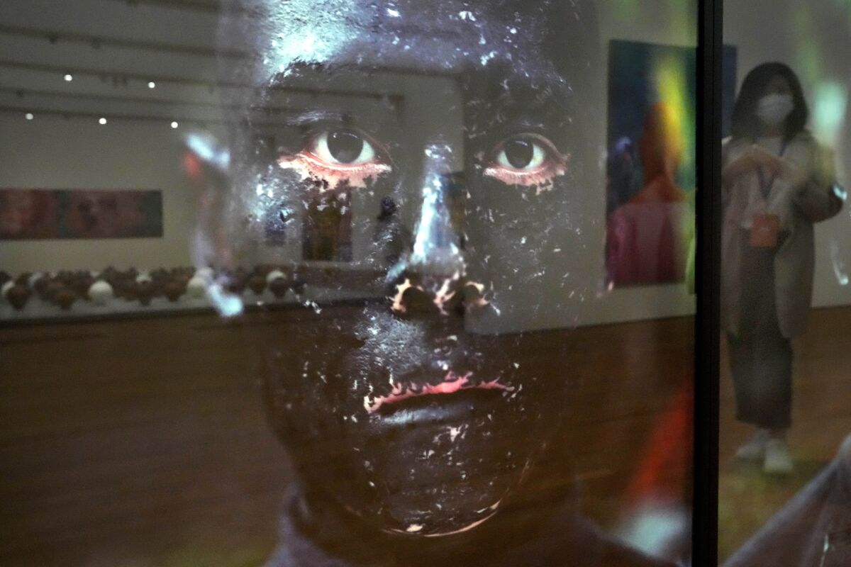 A woman is reflected by a glass framed photograph titled "Family tree" created by Chinese artist Zhang Huan during a media preview in the West Kowloon Cultural District of Hong Kong, Thursday, Nov. 11, 2021. Hong Kong's swanky new M+ museum, Asia's largest gallery with a billion-dollar collection, is set to open on Friday amid controversy over politics and censorship. (AP Photo/Kin Cheung)