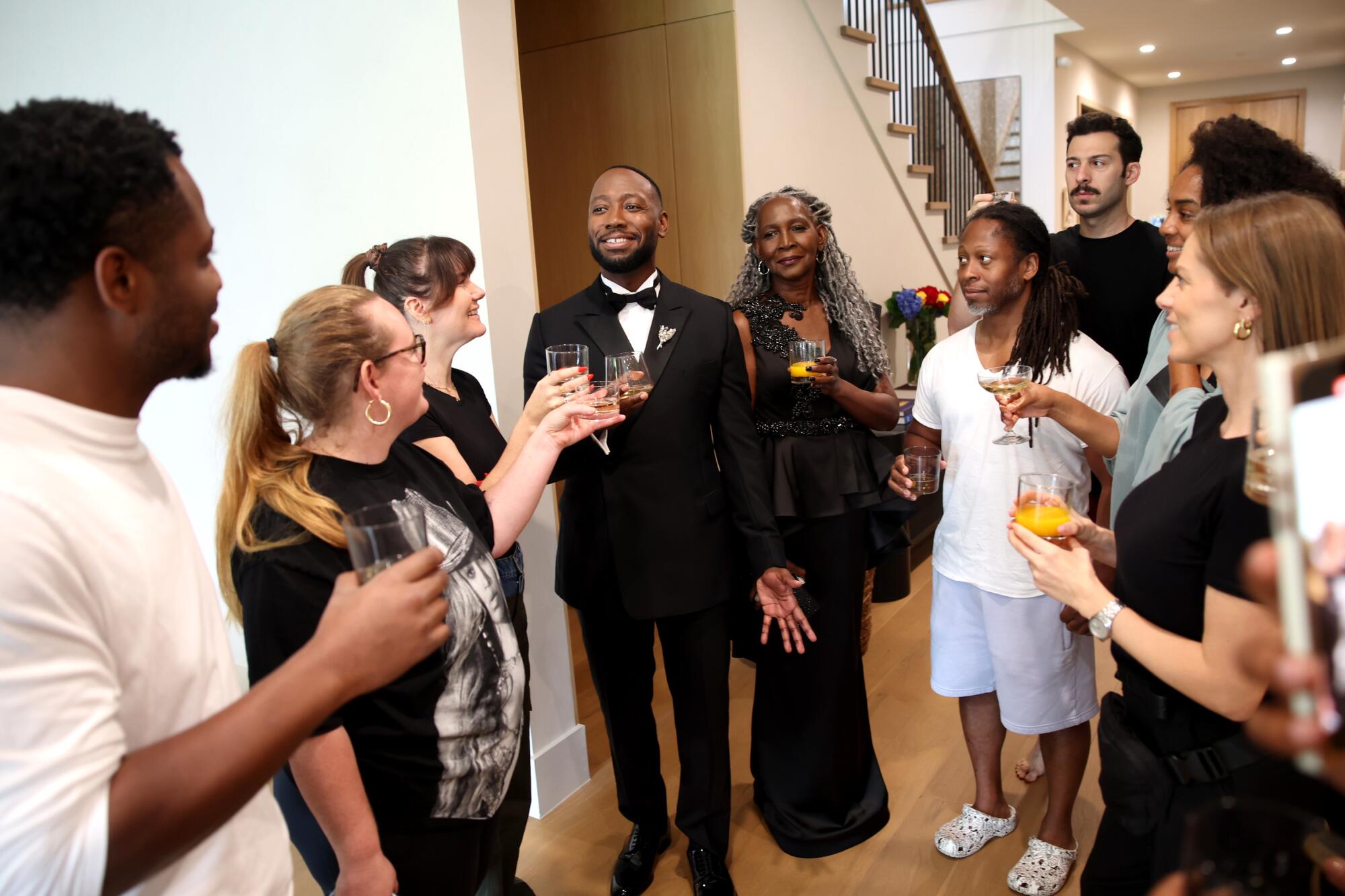 A group of people holding raised glasses a man in a tuxedo and woman in a dark dress walk into the room.