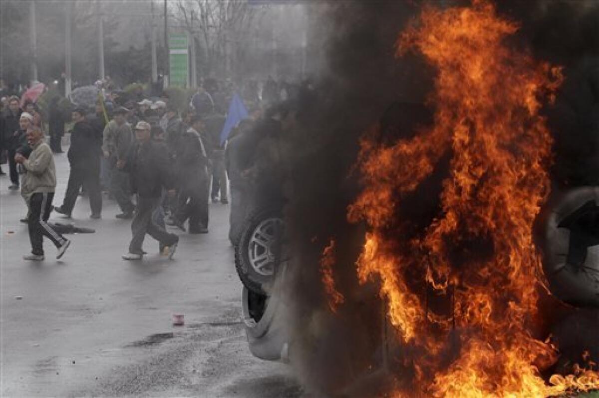 Protestors stand near a burning vehicle during clashes with police near the main government buildings in Bishkek, Kyrgyzstan, Wednesday, April 7, 2010. Police in Kyrgyzstan opened fire on thousands of angry protesters who tried to seize the main government building amid rioting in the capital as protests spread across the Central Asian nation. (AP Photo/Ivan Sekretarev)