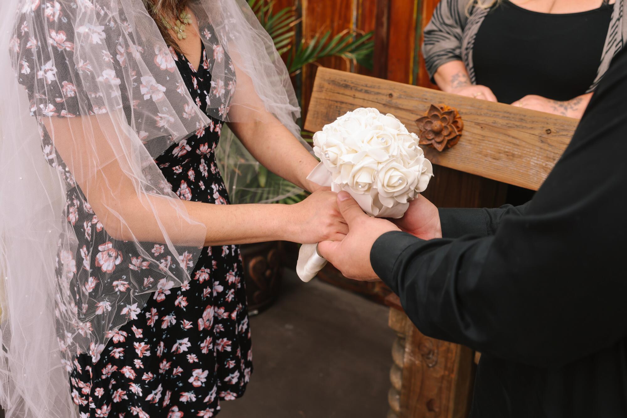 A couple hold hands and a bouquet of flowers during their wedding ceremony