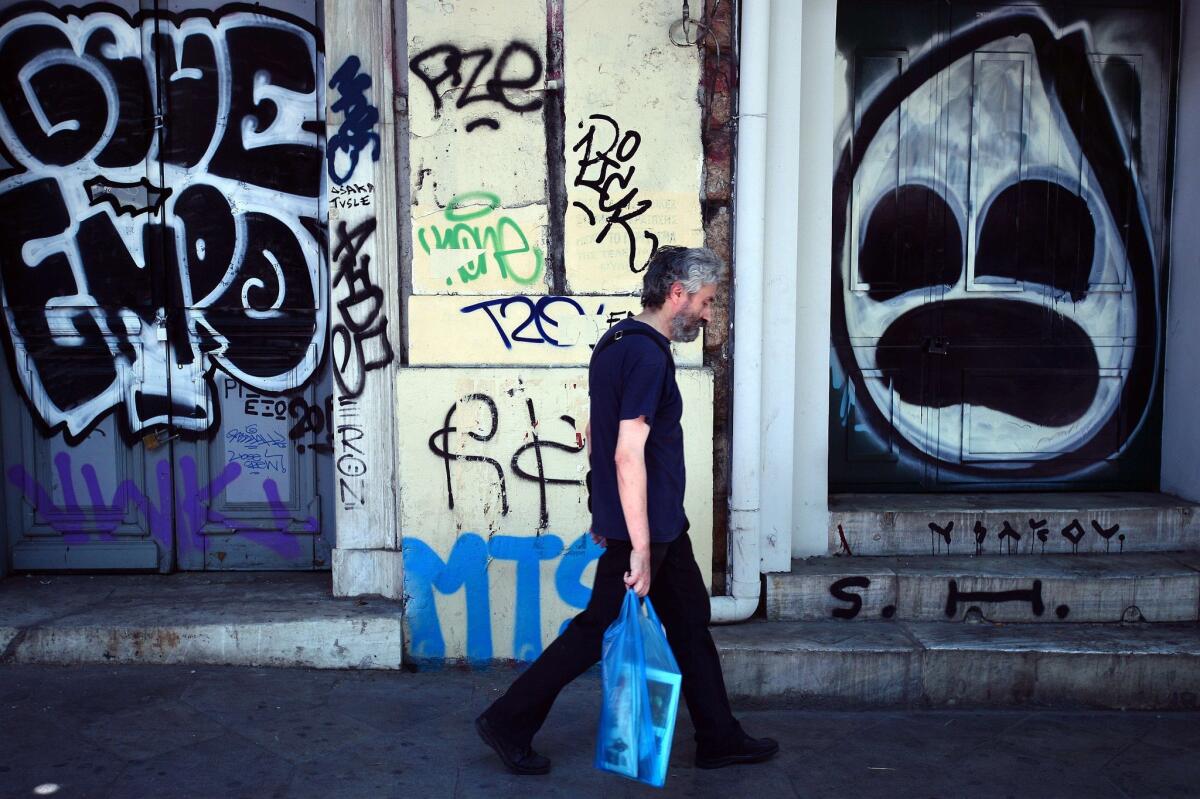 A man walks past stores shut down and covered with graffiti Tuesday in central Athens. Technical details of Greece's third bailout were reportedly agreed upon in talks during the day.