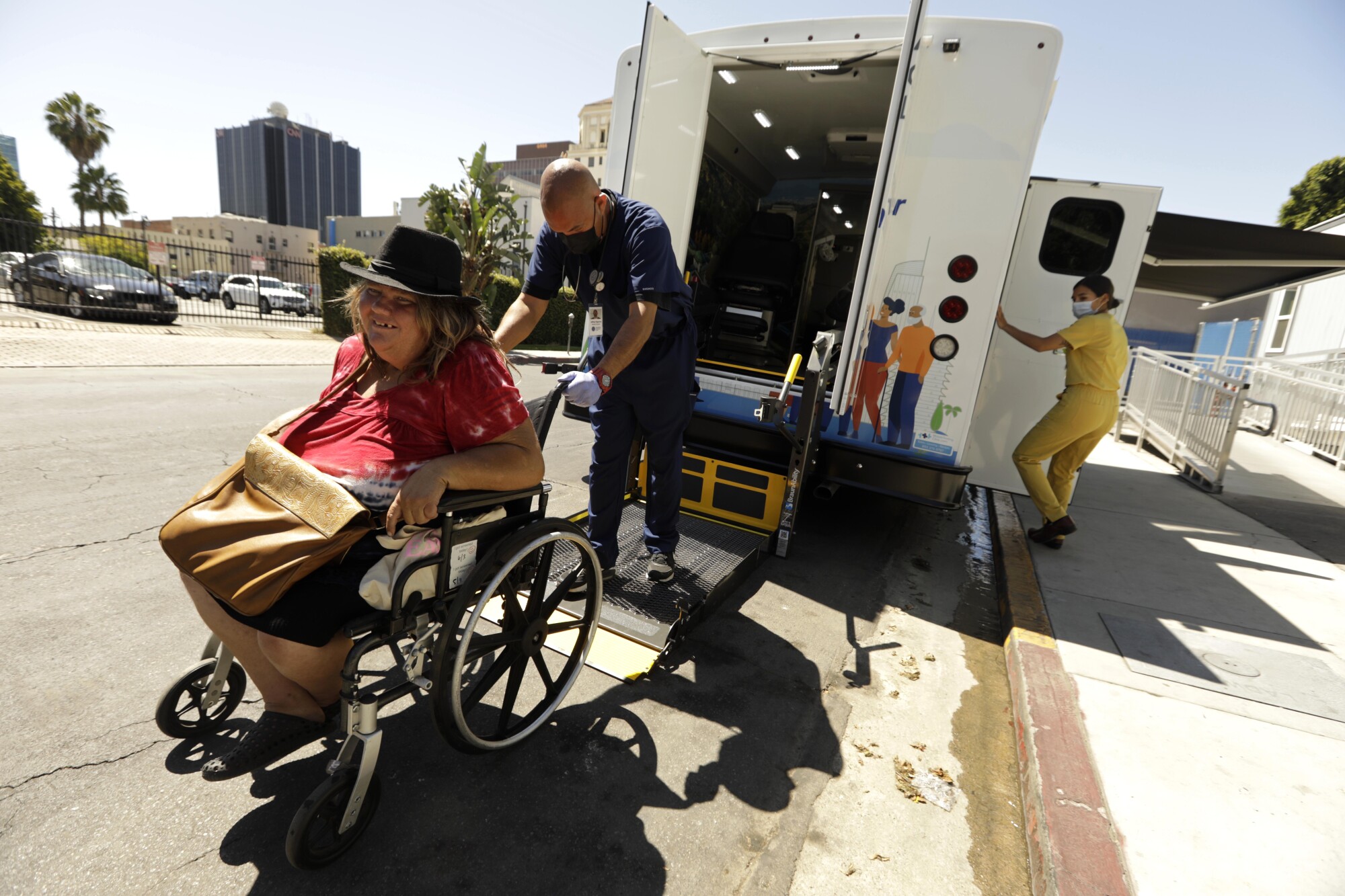 A medical assistant guides a homeless woman using a wheelchair onto the lift of the Saban Community Clinic mobile vehicle.