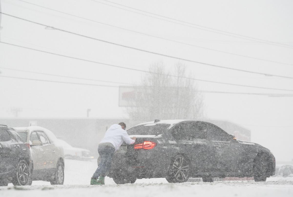 A person is behind a car on a snow-covered road.