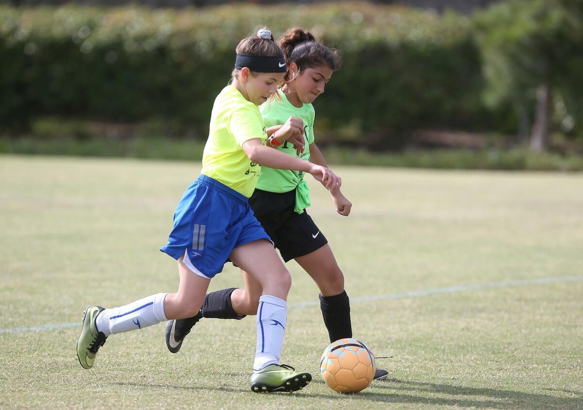 Newport Coast Elementary's Gianna Macafee, in blue shorts, moves the ball upfield as a Pegasus player comes in to defend during a girls' fifth- and sixth-grade Silver Division pool-play match at the Daily Pilot Cup on Friday at Jack R. Hammett Sports Complex in Costa Mesa.