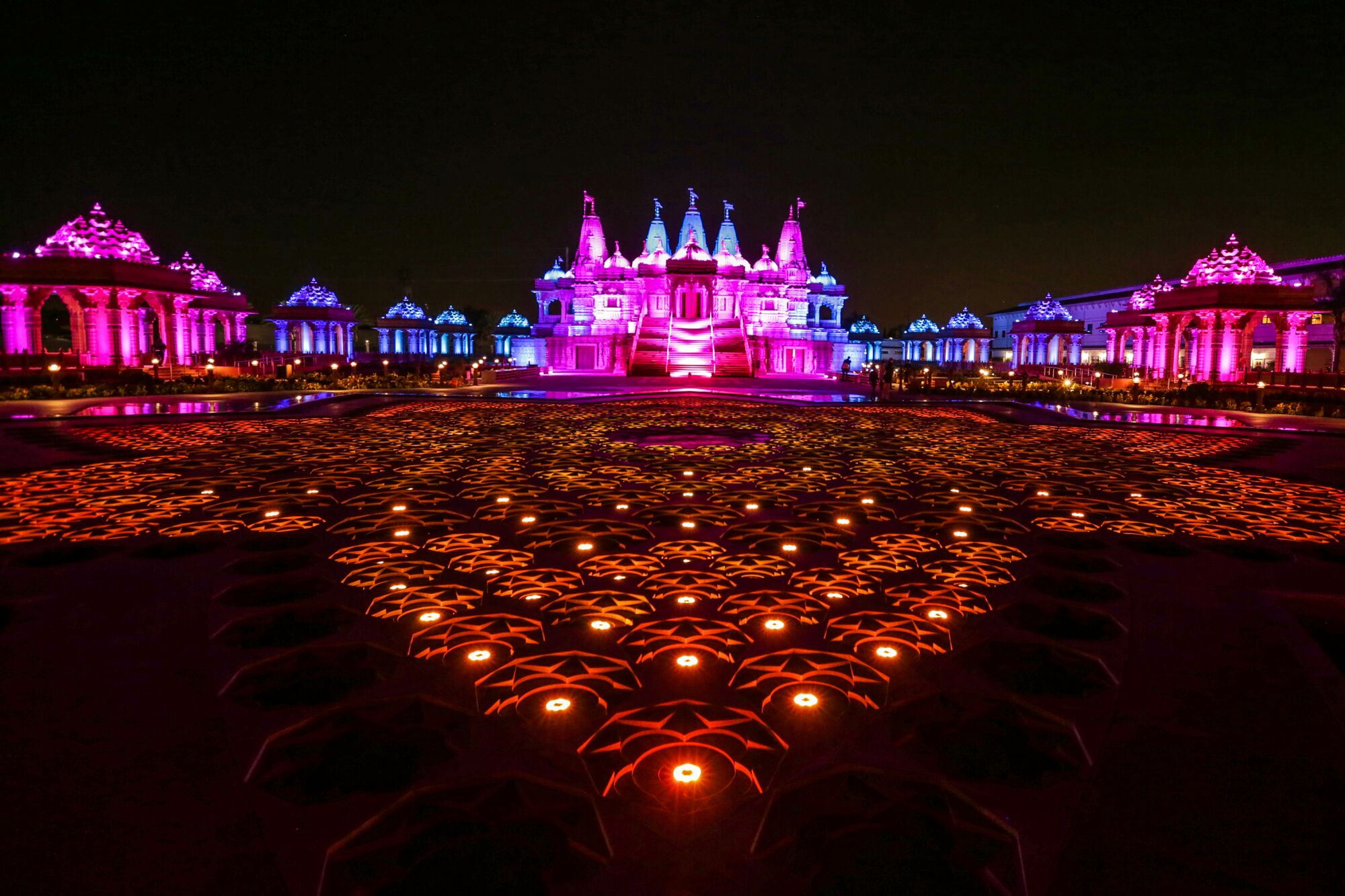Blue, purple, and red light bathes the exterior of a large, ornate Hindu temple at night.