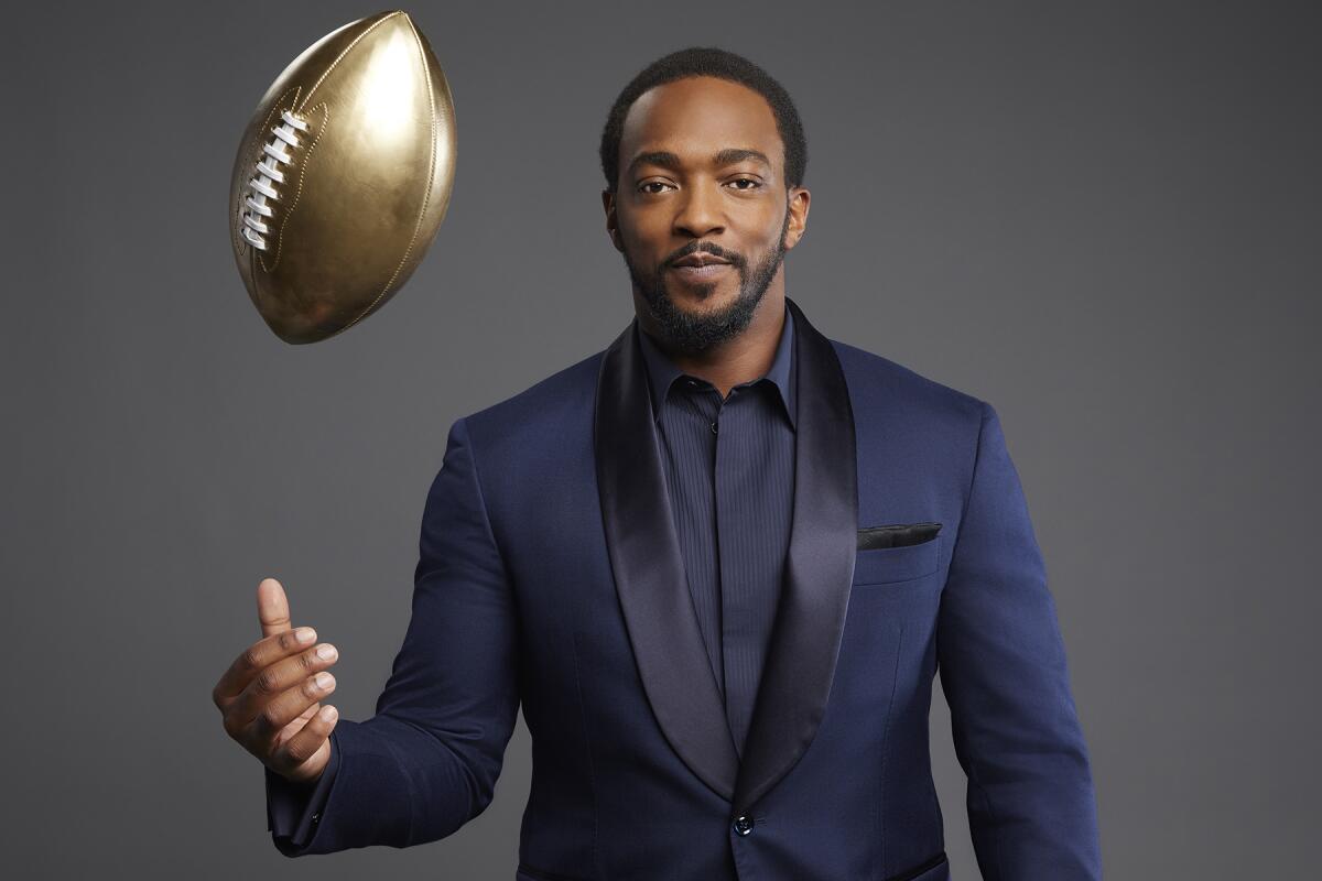 A tuxedoed Anthony Mackie throws a gold-colored football in the air.
