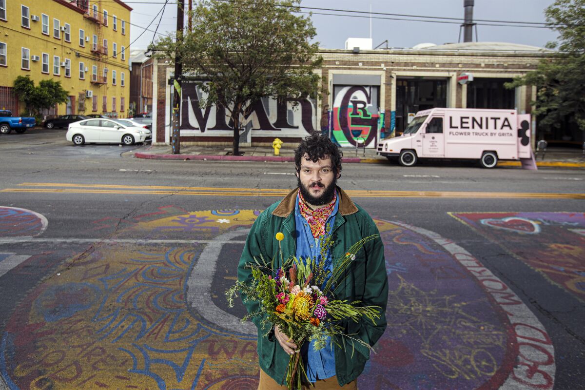 Nemuel DePaula stands on a street covered in graffiti art, holding a bouquet, his flower truck in the background.