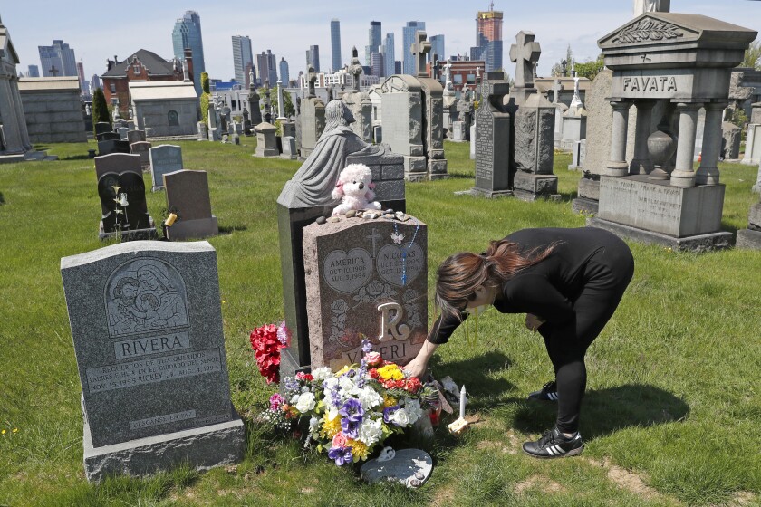 A woman tends to flowers and other items left at a grave.