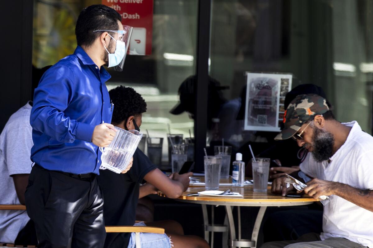 Un mesero usa una mascarilla mientras atiende a los comensales en un restaurante en California.