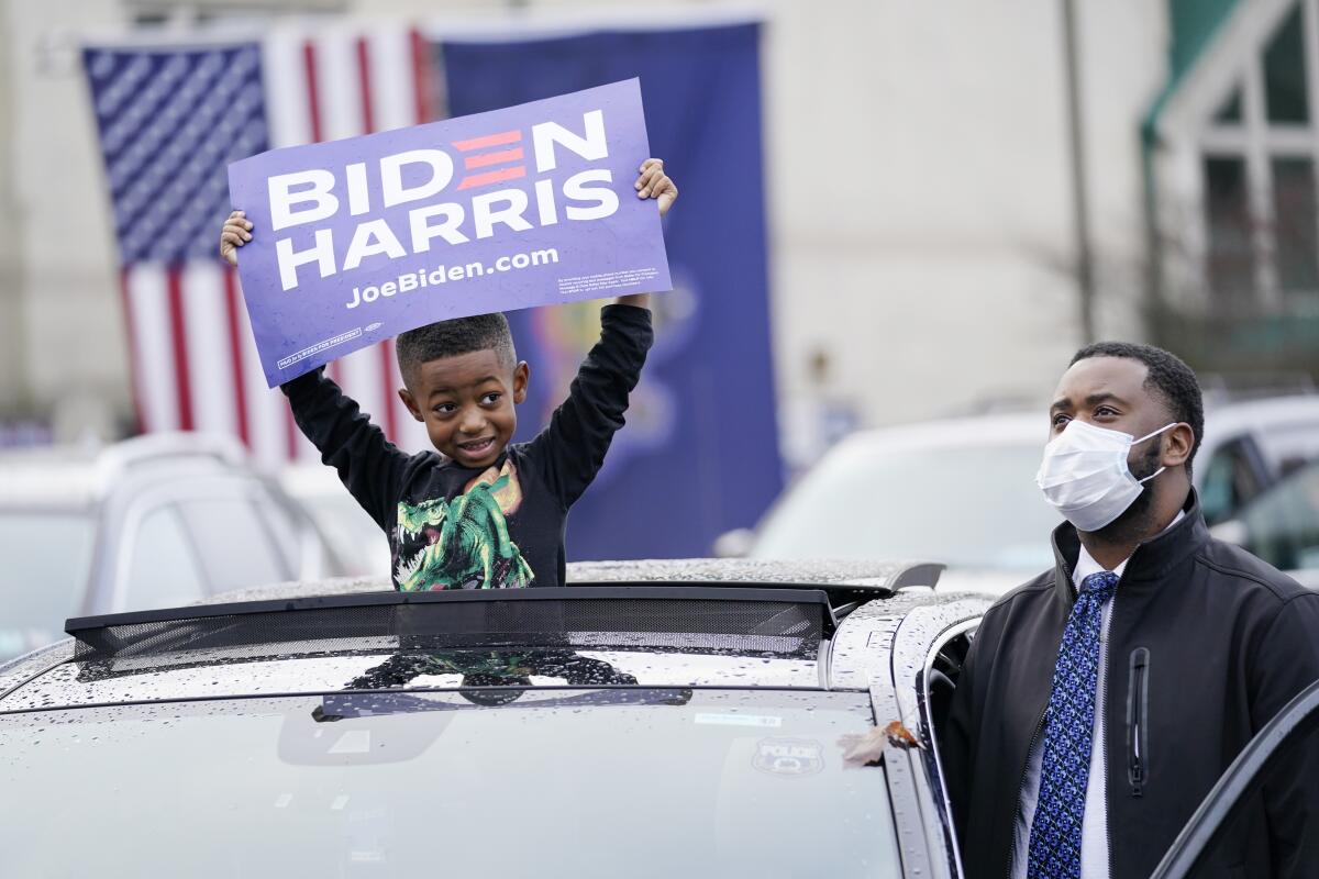 A young boy, through a car's sunroof, holds a Biden-Harris campaign sign.