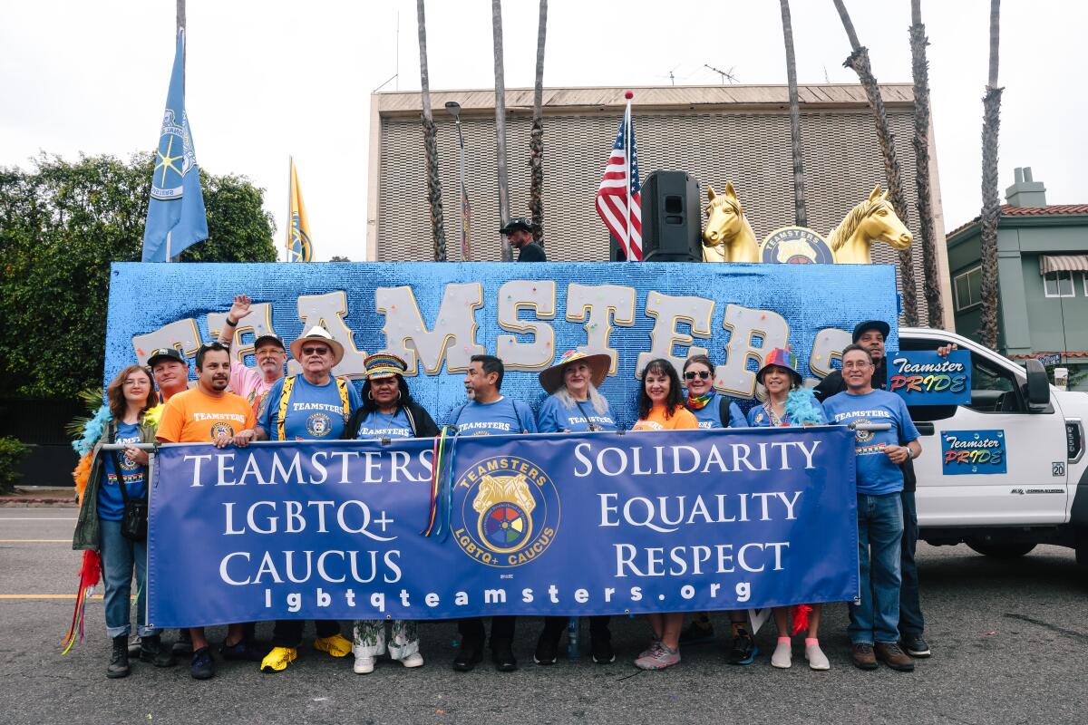 People in blue and orange T-shirts holding a large banner in front a sparkly blue parade float that says "Teamsters"