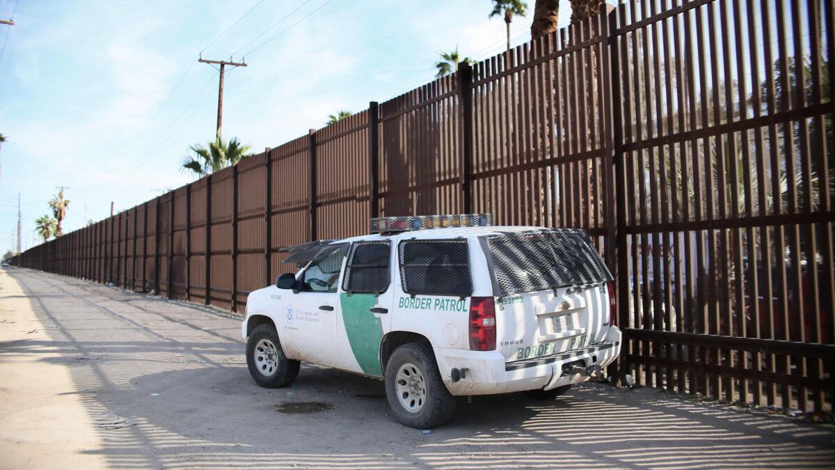 A Border Patrol agent looks over the wall in Calexico. A barrier built in the 1990s from recycled metal scraps and landing mat will be torn down for bollard-style posts that are 30 feet high.