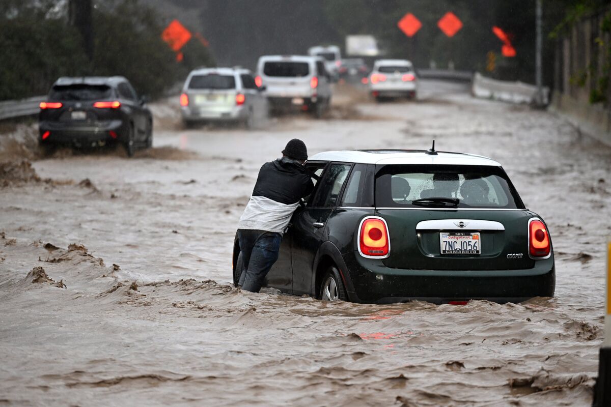 James Claffey pushes his stalled car from the southbound Highway 101 Freeway in Montecito on Jan. 9, 2023.