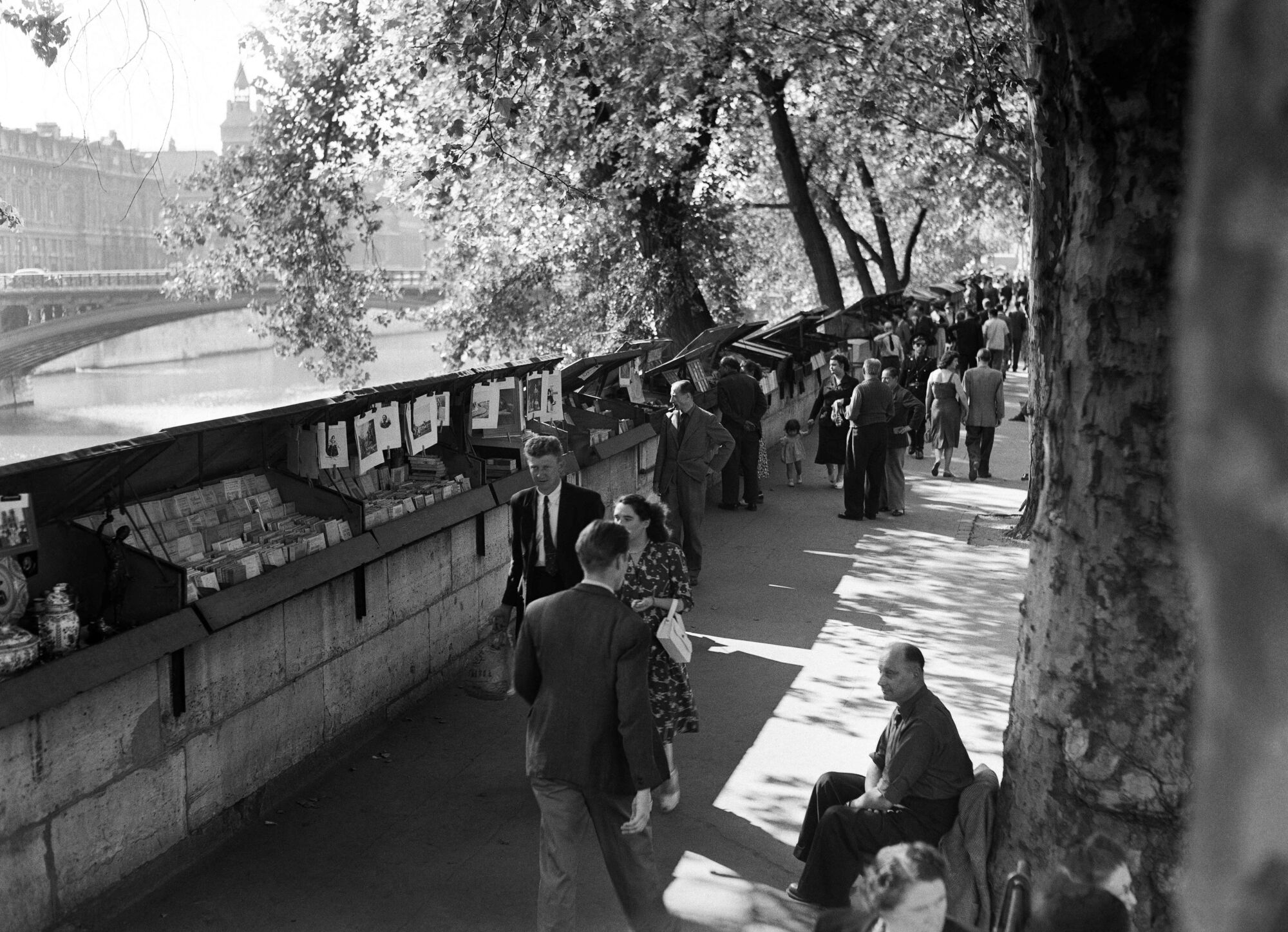 Parisians and tourists strolling along the banks of the Seine river in a black-and-white photo.