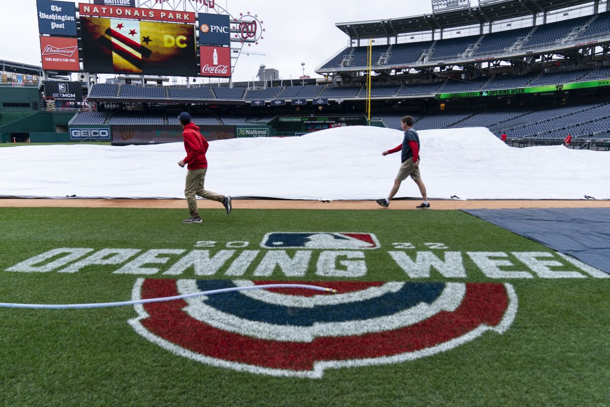 Members of the grounds crew roll up the tarp before baseball workouts at Nationals Park, Wednesday, April 6, 2022, in Washington. The Washington Nationals and the New York Mets are scheduled to play on opening day, Thursday. (AP Photo/Alex Brandon)