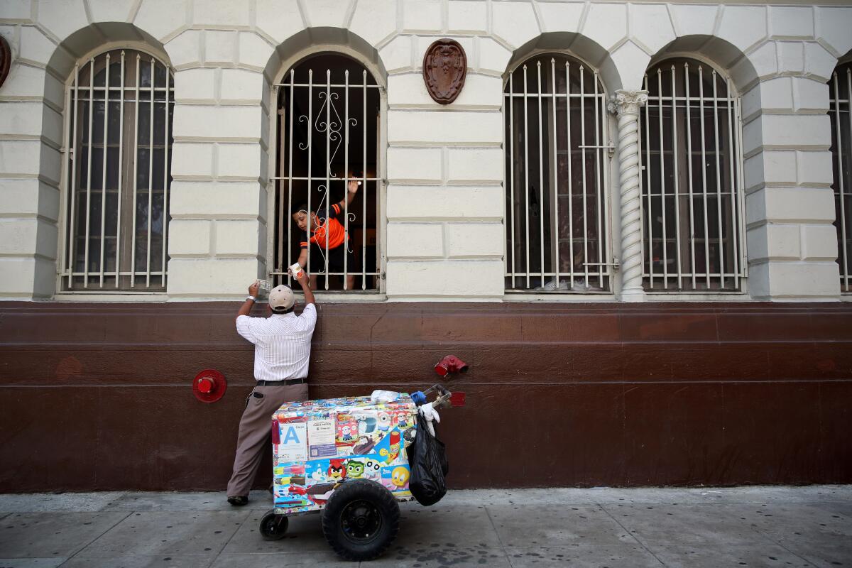 A man hands ice cream to a customer through a window from his cart on the sidewalk below.