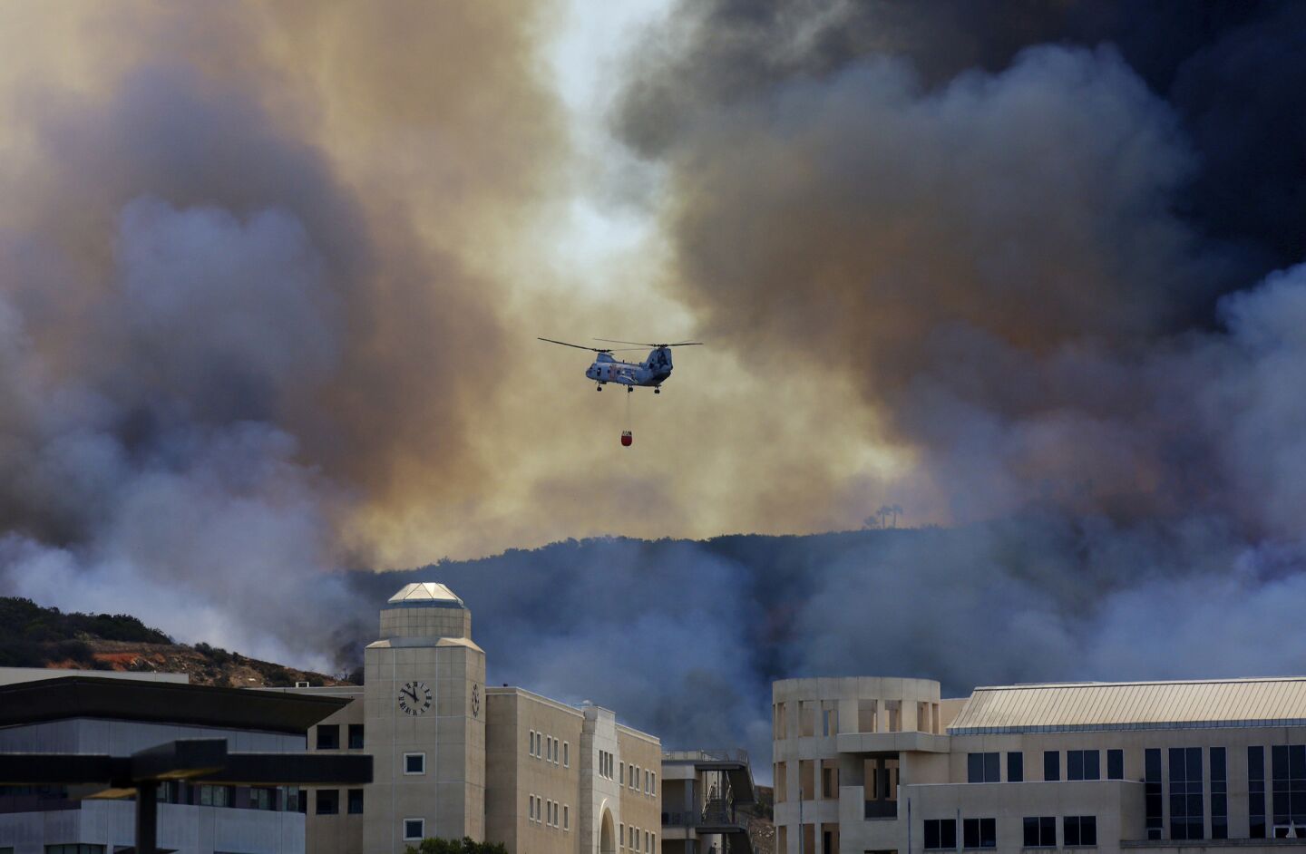 Smoke billows above the Cal State San Marcos campus as water-dropping helicopters battle the Cocos fire.