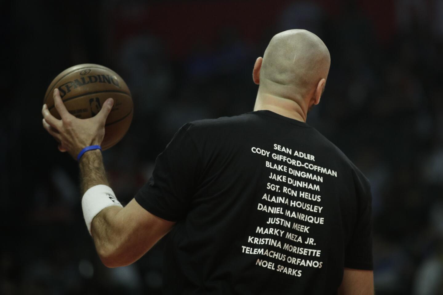 Los Angeles Clippers' Marcin Gortat wears a T-shirt bearing the names of the 12 victims killed in Wednesday night's shooting at a country bar in Thousand Oaks, Calif., before the team's NBA basketball game against the Milwaukee Bucks Saturday, Nov. 10, 2018, in Los Angeles. (AP Photo/Jae C. Hong)