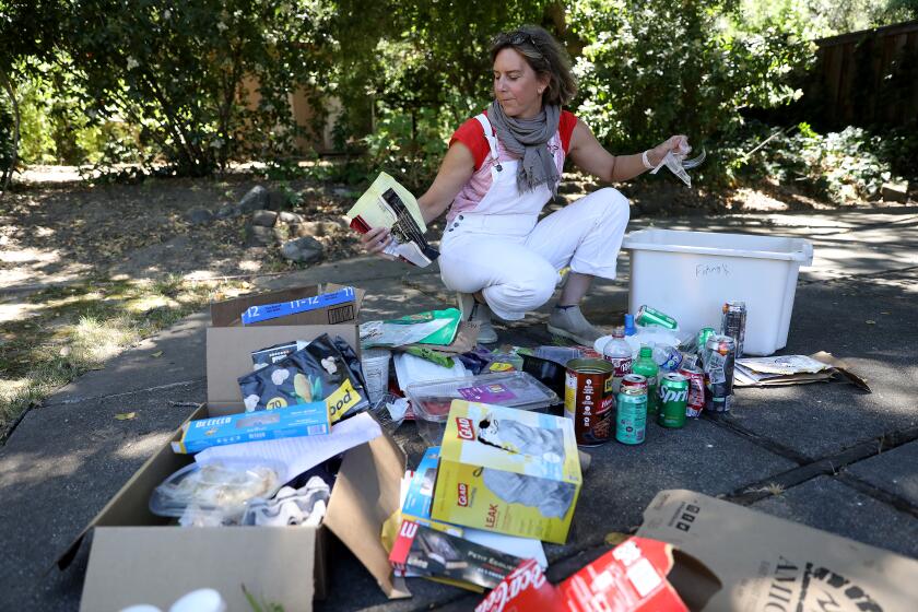 Susanne Rust wearing white overalls crouching down sorting groups of her family's trash on the ground outside her home
