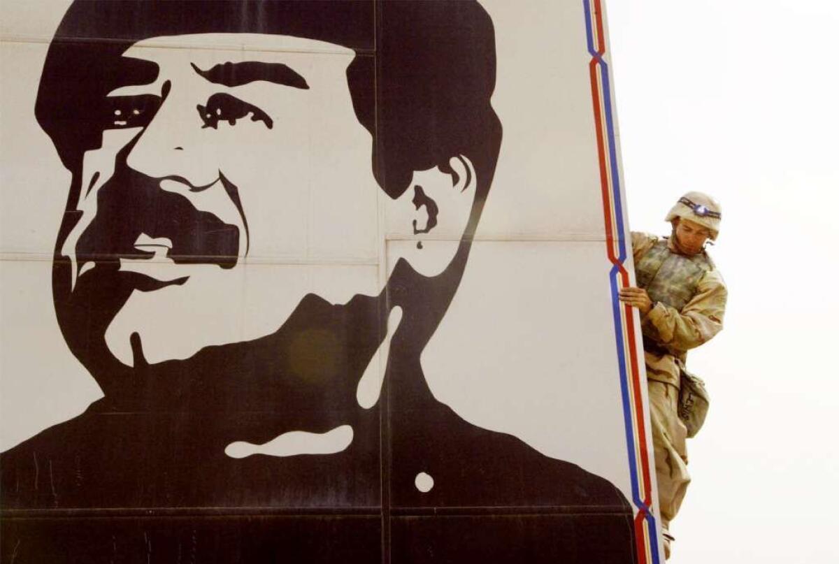 A U.S. Marine prepares to pull down a billboard of Iraqi ruler Saddam Hussein in  2003.