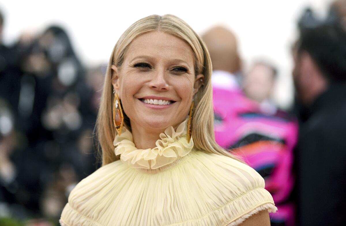 Gwyneth Paltrow smiles wearing a yellow ruffled gown and dangle gemstone earrings. 