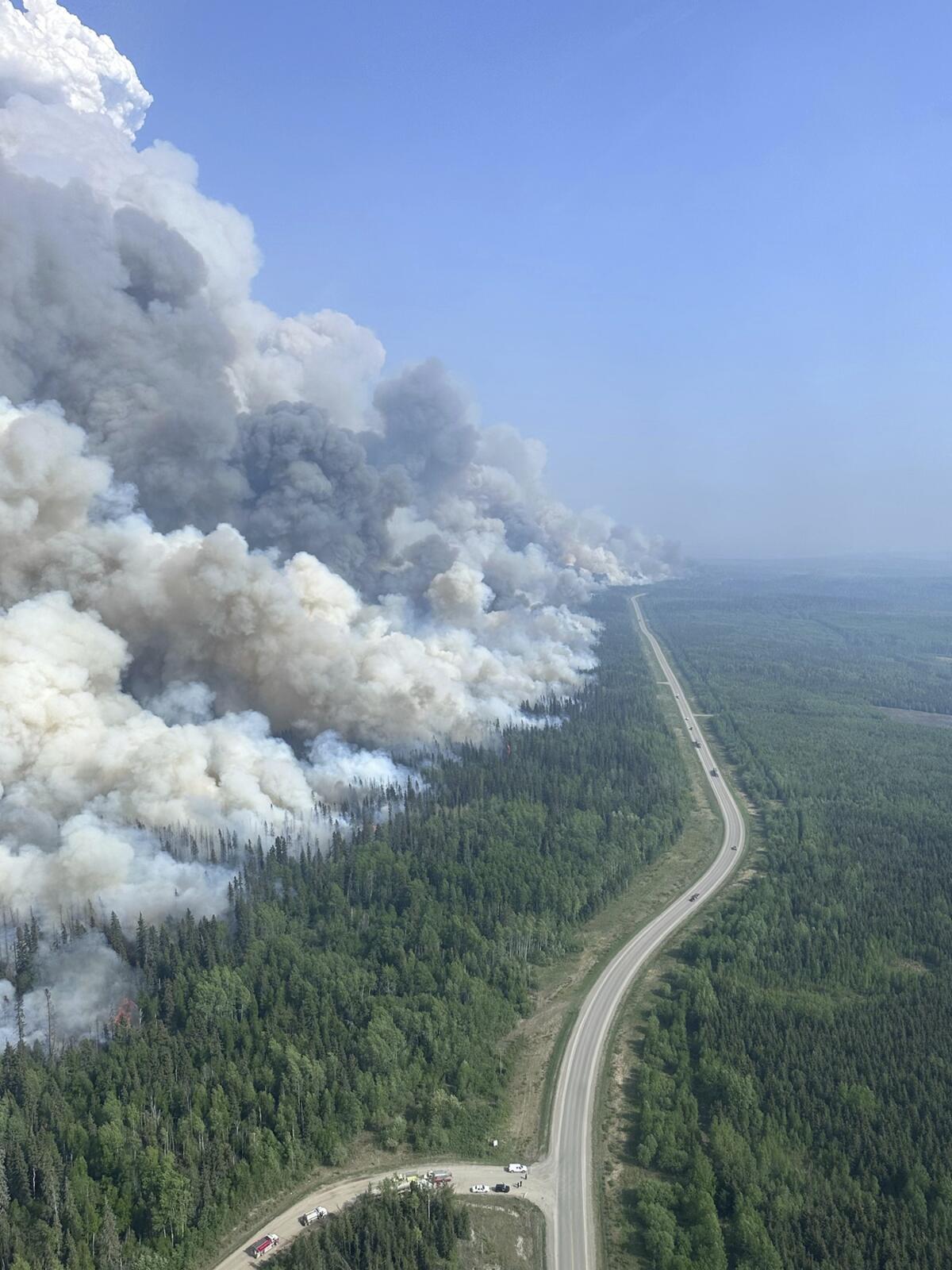 Smoke billows above a forested area with a roadway running through it
