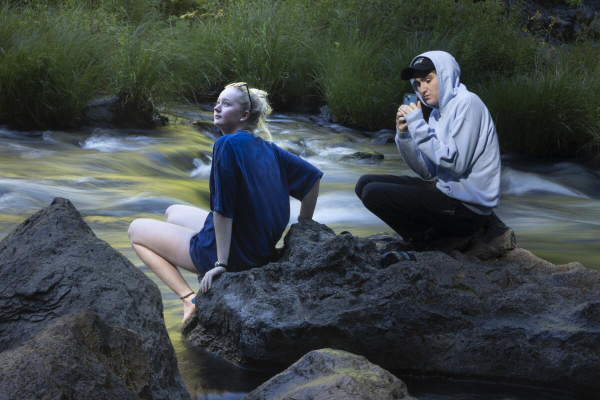 A young man and woman perch on a rock below Burney Falls. 