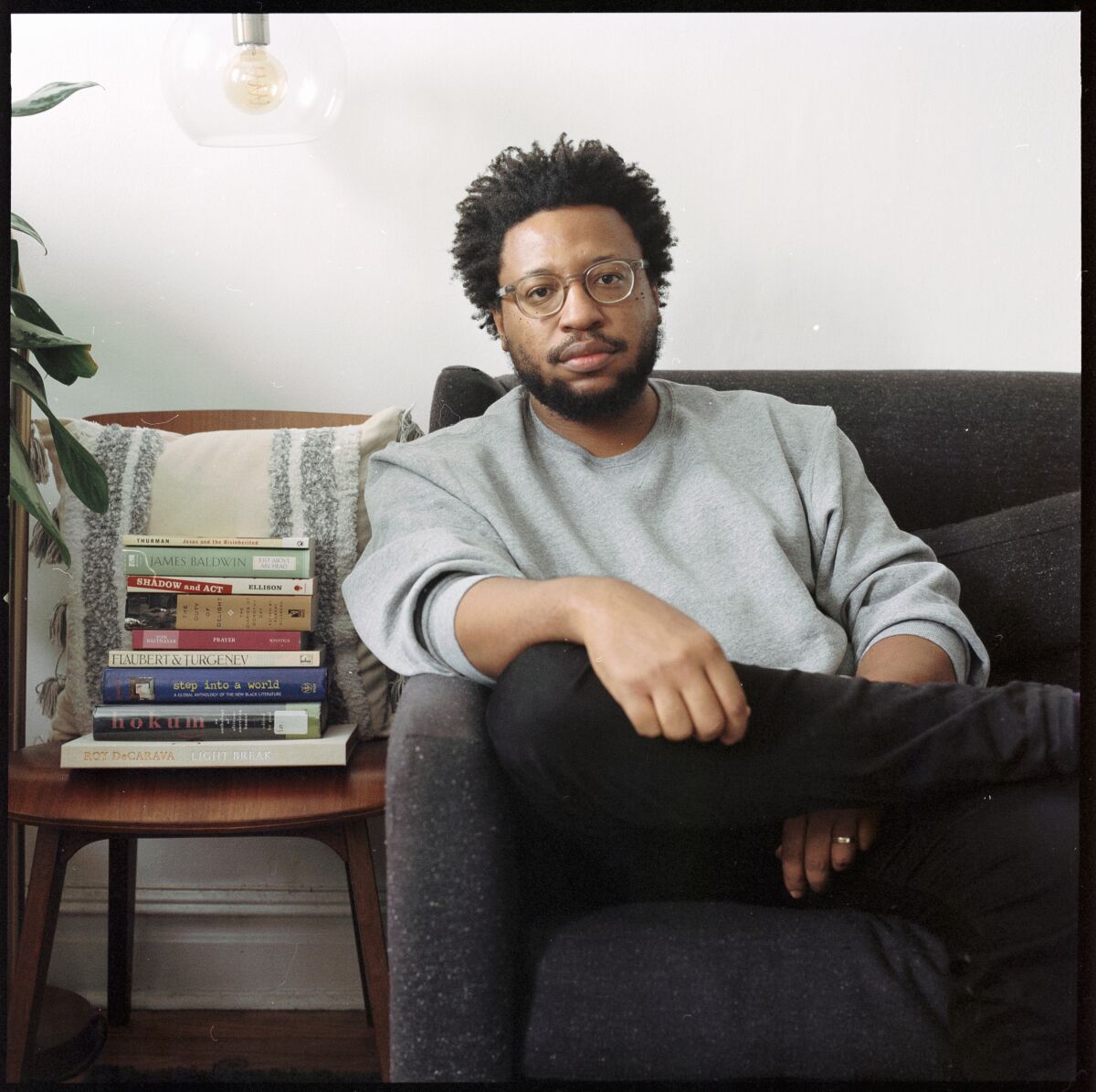 Vinson Cunningham sits on a couch next to a stack of books.
