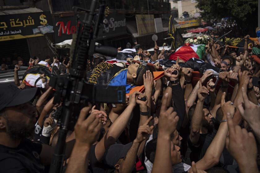 A gunman holds up his weapon as mourners carry the bodies of Palestinians, with some draped in the Islamic Jihad militant group flags, during their funeral in the West Bank city of Jenin, Thursday, May 23, 2024. The Israeli military said Thursday it has completed a two-day operation in the occupied West Bank that the Palestinian Health Ministry says killed 12 Palestinians. Militant groups claimed at least eight of the dead as fighters, one from Hamas and seven from the Al-Aqsa Martyrs Brigade. (AP Photo/Leo Correa)