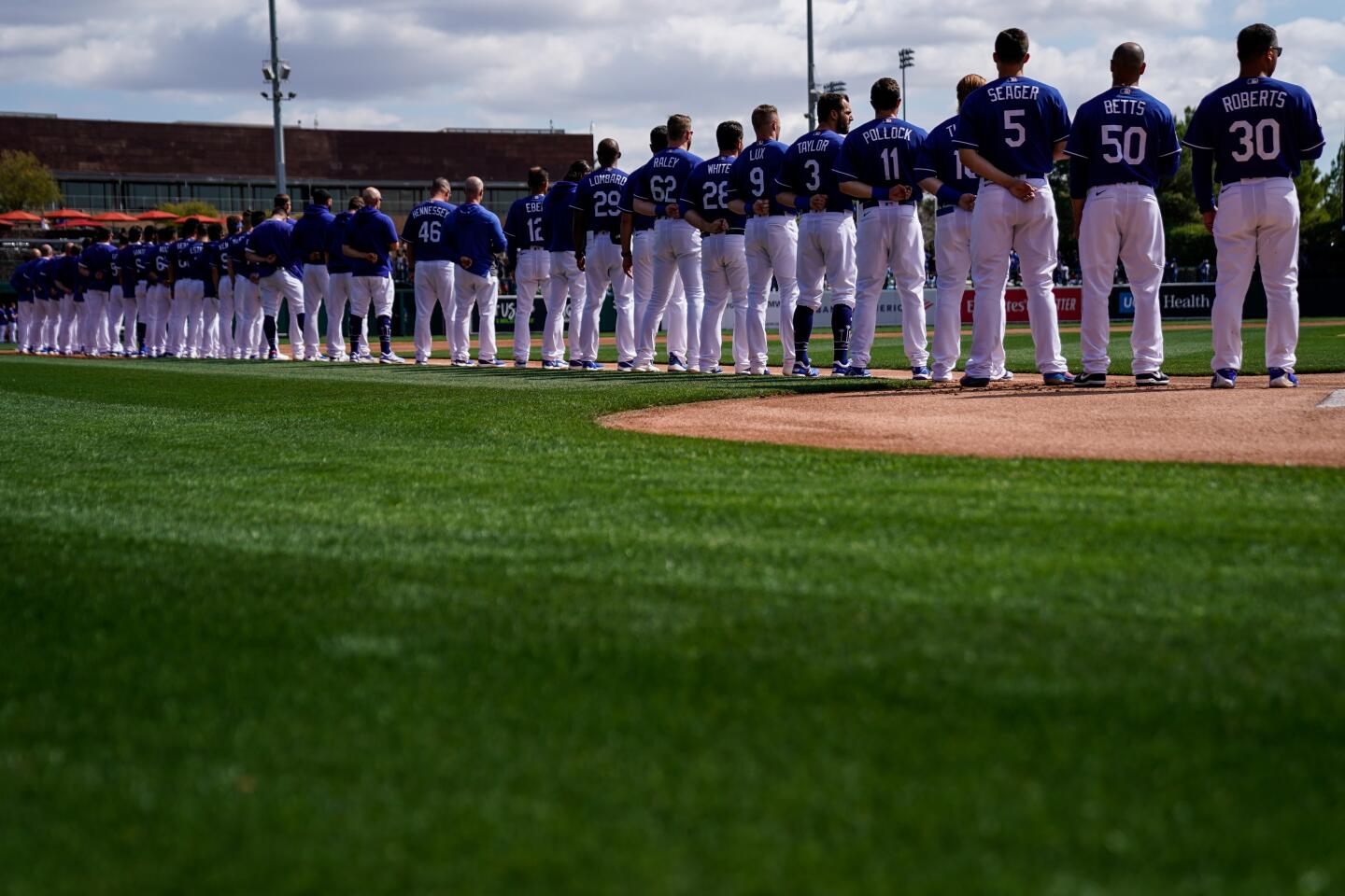 Dodgers players stand along the third base line during the singing of the national anthem before an exhibition game against the Chicago Cubs at Camelback Ranch on Feb. 23, 2020.