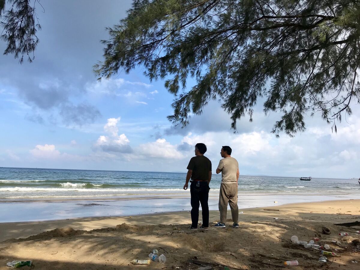 Two Chinese nationals stand on the litter strewn Otres Beach in Sihanoukville, Cambodia. An influx of Chinese investors has transformed the once sleepy coastal city, but a deadly June 22 building collapse has renewed questions about the quality of Chinese construction and the Cambodian government's close ties to Beijing