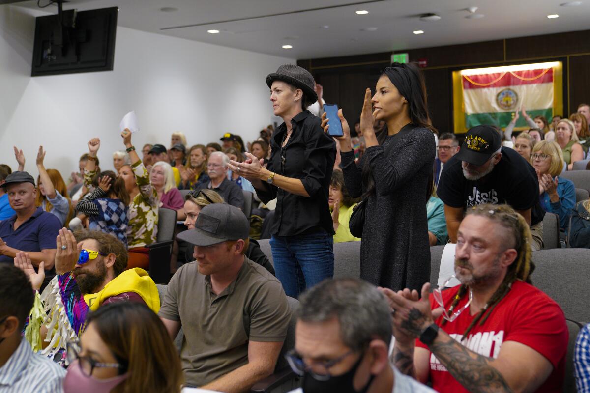 Audience members stand, clap and raise their hands at San Diego County supervisors meeting