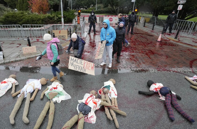 Women hold posters near mannequins covered in fake blood.  