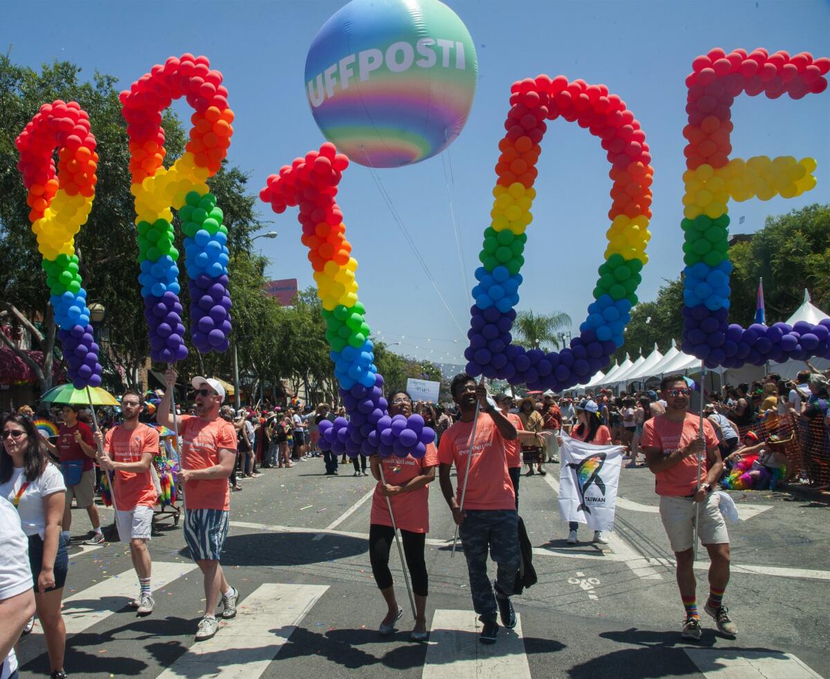 Parade participants carry a giant, rainbow-colored balloon letters spelling "Pride."
