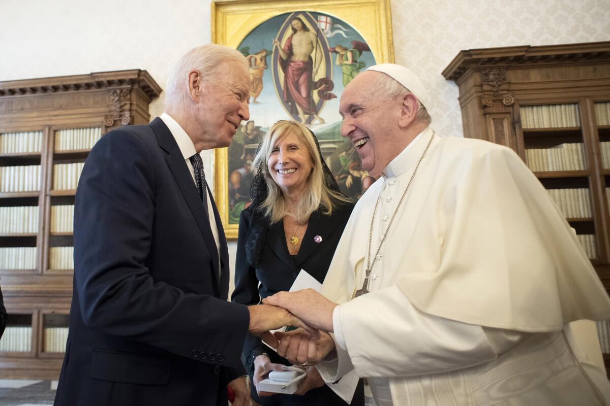Pope Francis greets Joe Biden as an unidentified woman looks on 