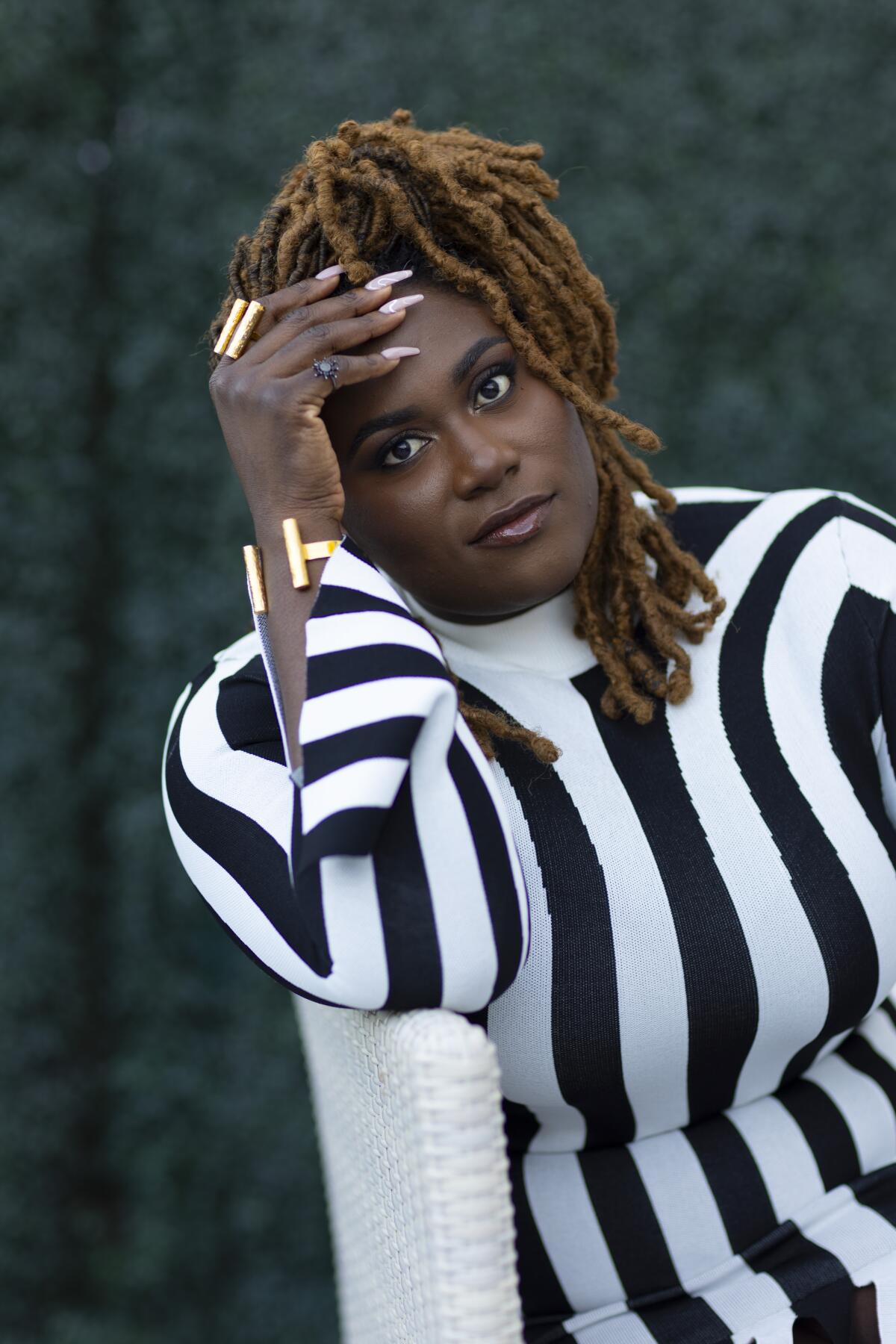 Danielle Brooks wears a black-and-white striped outfit as she sits sideways on a chair for a portrait.