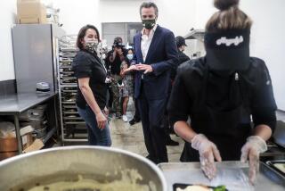 In this April 2021 photo, Elva Quinonez prepares food as Gov. Gavin Newsom talks with Magaly Colelli at Magaly's restaurant