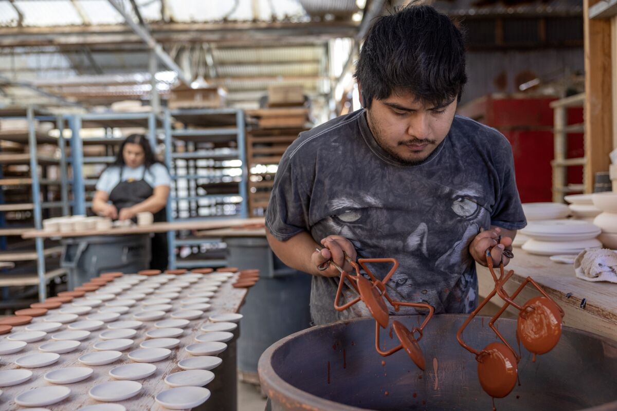 Noel Mendoza dips soy dishes into a tub of glaze at The Wheel.