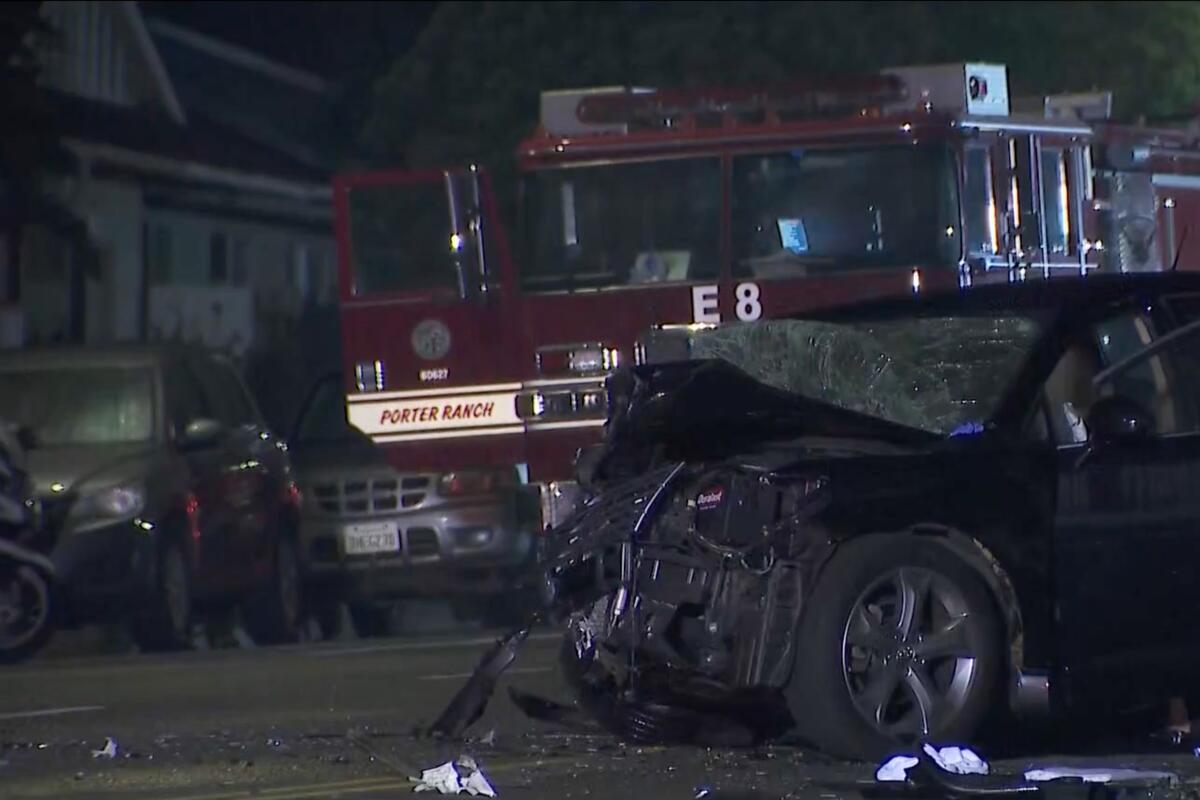 An SUV with a completely mangled front end sits in the street amid debris in front of a firetruck.
