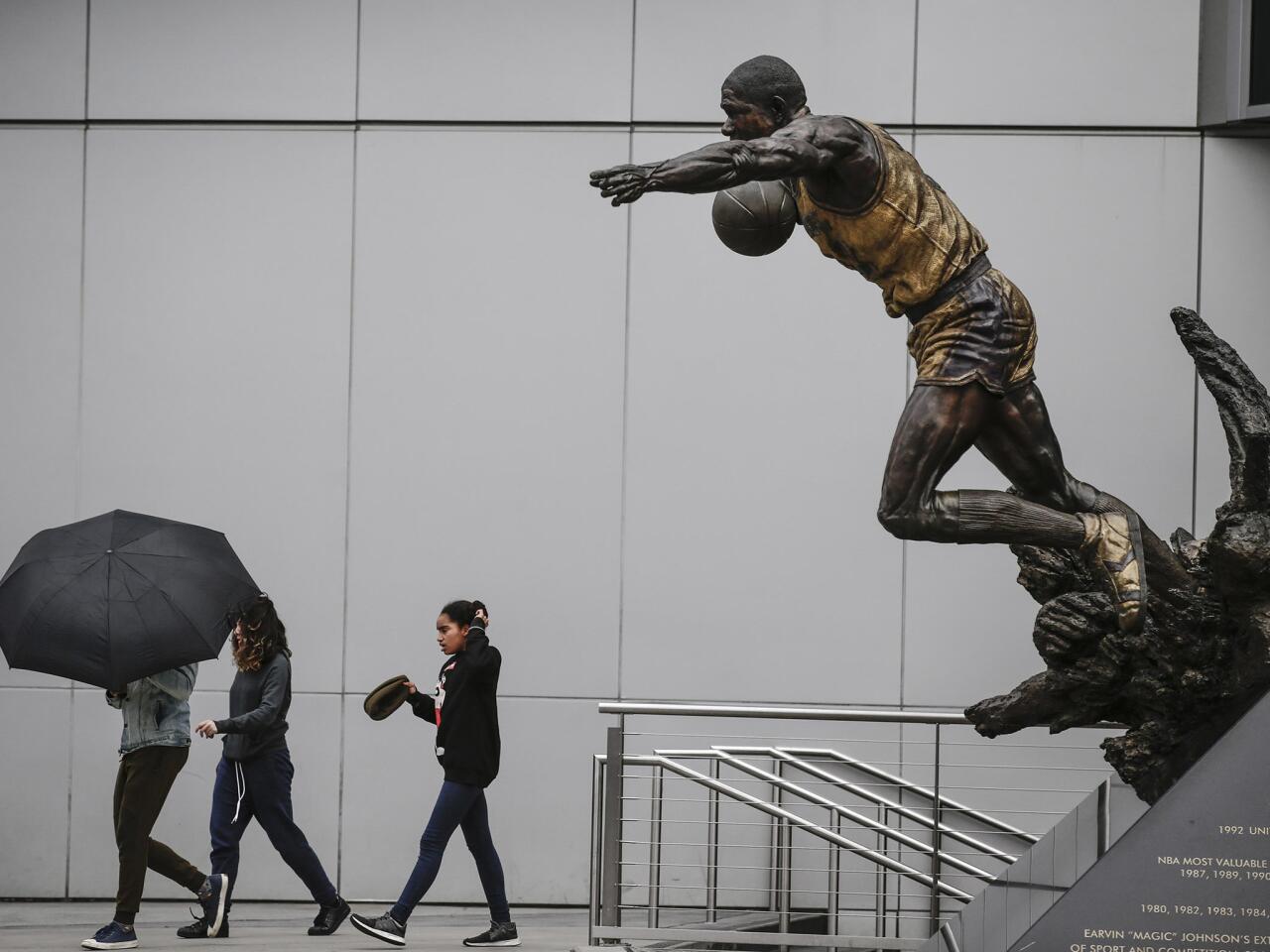 Pedestrians pass a statue of Magic Johnson leaning into a blustery wind outside Staples Center in downtown Los Angeles on Wednesday.