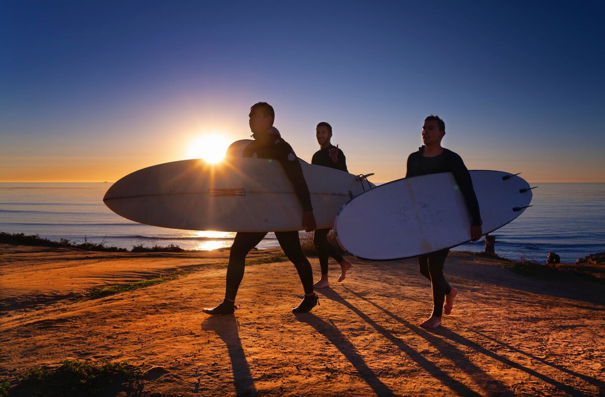 A small group of surfers return from surfing below the cliffs at Sunset Cliffs in Ocean Beach.