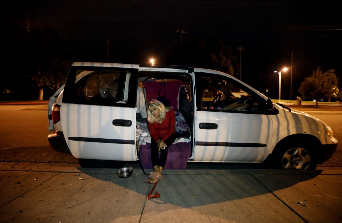 In the San Gabriel Valley, 70-year-old Andrea Colucci sits in the doorway of the van she and her dog are living in.