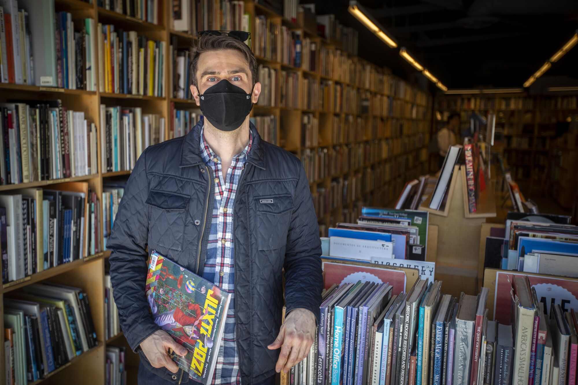 A man wearing a quilted jacket and a face mask in a bookstore.