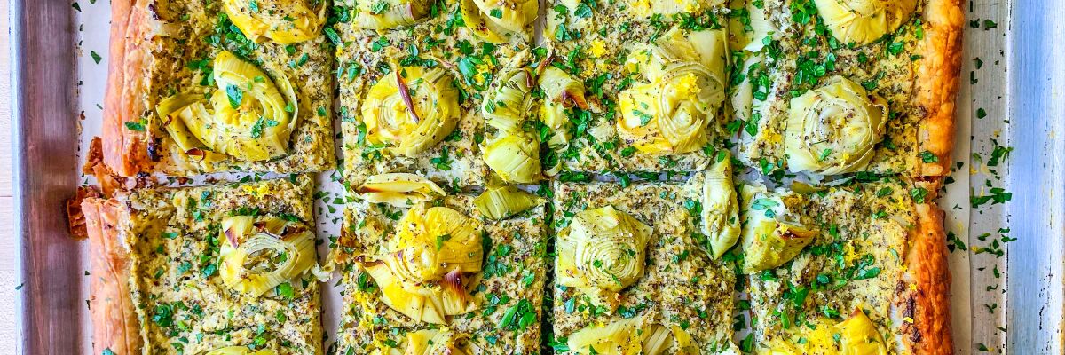 A tray holds a tart made of puff pastry topped with artichoke hearts and fresh herbs.
