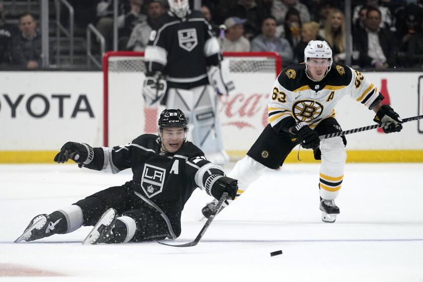 Los Angeles Kings right wing Dustin Brown, left, passes the puck after falling as Boston Bruins left wing Brad Marchand skates behind during the second period of an NHL hockey game Monday, Feb. 28, 2022, in Los Angeles. (AP Photo/Mark J. Terrill)